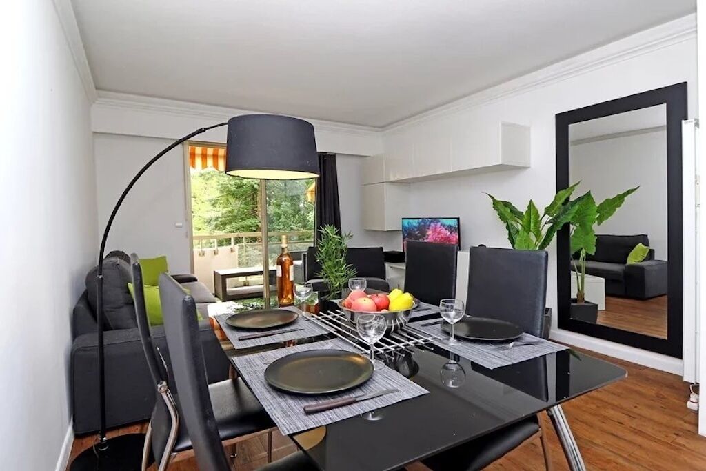 A dining area with a table set for four, a black lamp, and a large mirror reflecting the room.