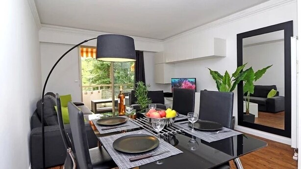 Un coin repas avec une table dressée pour quatre personnes, une lampe noire et un grand miroir qui reflète la pièce.