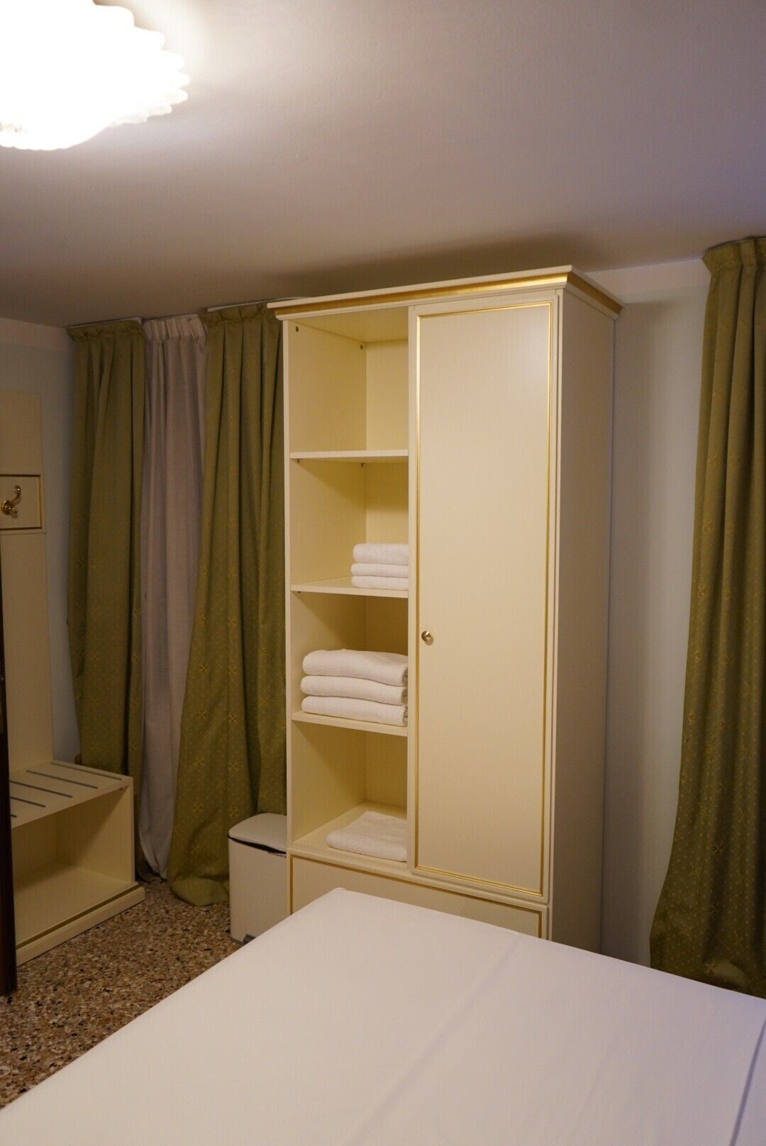 A room with a bed, a wardrobe with shelves, and a small table.