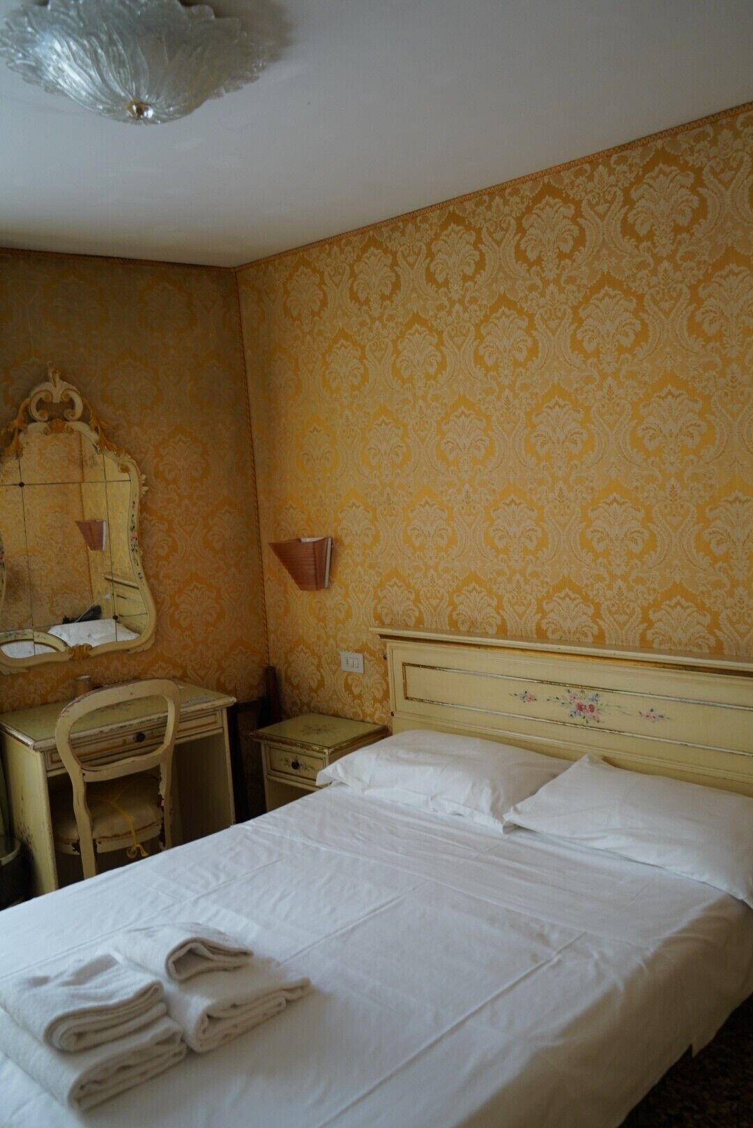Een hotelkamer met een bed, een bureau, een stoel, een spiegel en een wandklok.