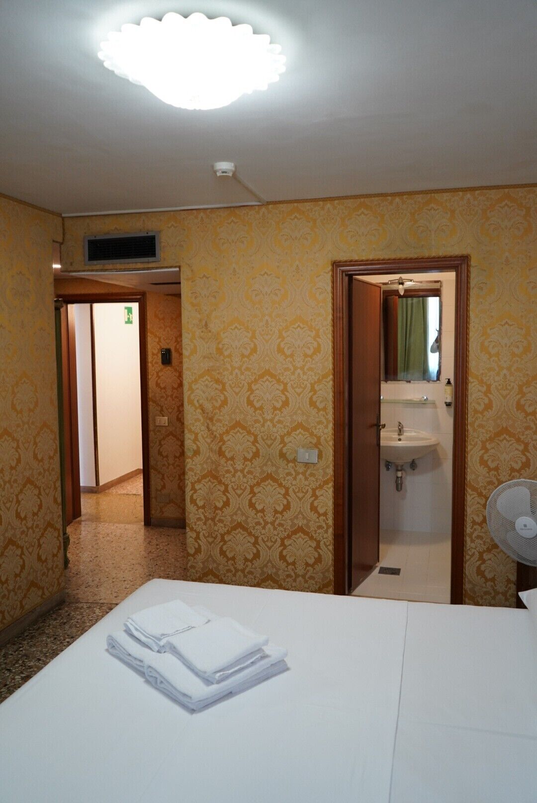 A hotel room with a bed, a bathroom with a sink and mirror, and a fan.