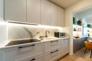 A modern kitchen with white cabinets, a marble backsplash, a black induction cooktop, a built-in microwave, and a sink with a faucet. - Genteel Home Campuccio Firenze (Florence)