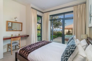 A bedroom with a bed, a desk, a chair, a window with curtains, and a view of the outdoors.