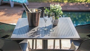 Ein Tisch am Pool mit einem Metallkübel, zwei Weingläsern und einem Blumentopf.