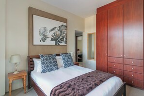 A neatly made bed with patterned pillows, a wooden nightstand with a lamp, a large mirror, and a wardrobe with multiple drawers. - Delightful unit with 3 bed, 3 bath & pool make this an ideal home to relax. (Knysna)