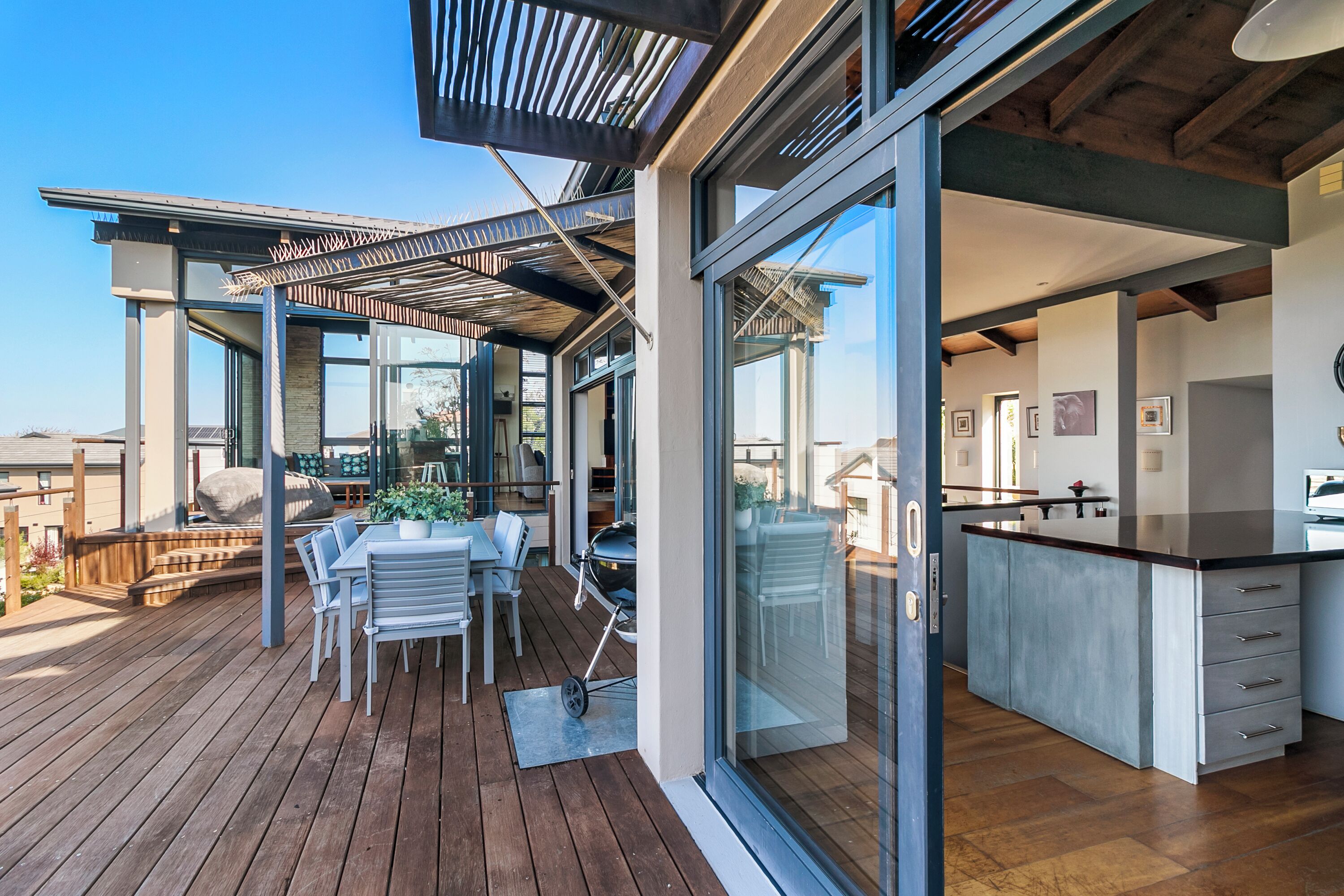 Une cuisine moderne dotée d’un grand îlot central, d’un coin repas avec des sièges extérieurs et d’une pergola surplombant la terrasse.