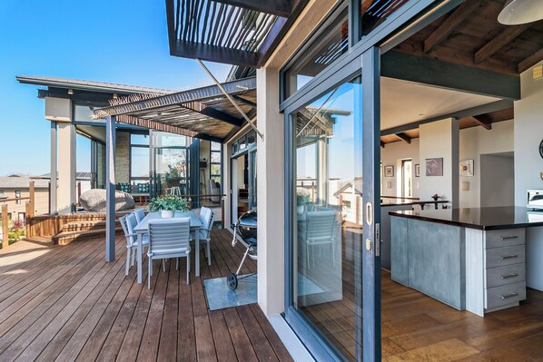 A modern kitchen with a large island, a dining area with outdoor seating, and a pergola over the patio. - Delightful unit with 3 bed, 3 bath & pool make this an ideal home to relax. (Knysna)