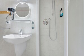A bathroom with a white sink, a mirror, a handheld hair dryer, and a shower with a handheld showerhead and a bottle of shampoo. - Apartment 'Venezia Baroque Charm' with Wi-Fi and Air Conditioning (Venice)