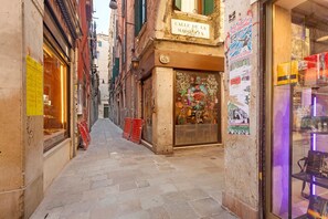 A narrow street with a shop on the right and a building with a sign above it. - Apartment 'Venezia Baroque Charm' with Wi-Fi and Air Conditioning (Venice)
