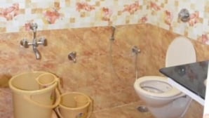 Baño con inodoro, lavamanos, ducha y secador de manos. Hay dos cubos en el suelo.