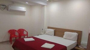 Una habitación de hotel con una cama, dos sillas rojas, una mesita de noche y un equipo de aire acondicionado.