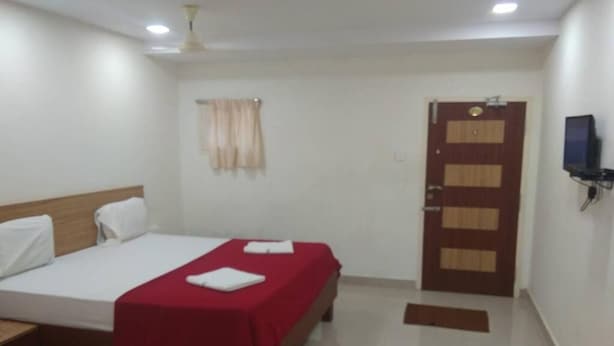 Habitación de hotel con cama, televisor montado en la pared, una puerta y ventana con cortinas.