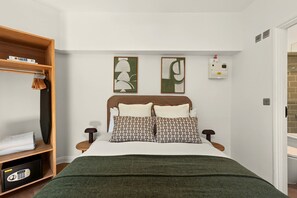 A neatly arranged bedroom with a bed, two pillows, a bedside table, a shelf with folded clothes, and two abstract wall art pieces. - GuestReady - Stylish Double En-Suite in London (London)