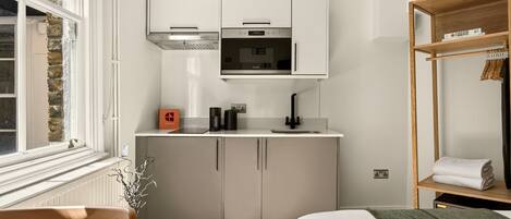 A compact kitchenette with a microwave, oven, and white cabinets.