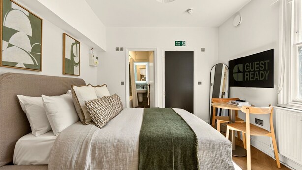 Een hotelkamer met een bed, een bureau, een spiegel, een bordje 'Nooduitgang' en een bordje 'Klaar voor gasten'.