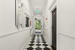 A hallway with a checkered floor, white walls, and a door with a red sign. - GuestReady - Stylish Double En-Suite in London (London)
