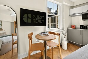 A modern room with a bed, a small round table with chairs, a 'GUEST READY' sign, a window, and a kitchenette. - GuestReady - Stylish Double En-Suite in London (London)