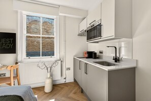 A modern kitchen with a built-in oven, a sink, and a window with a view of a brick wall. - GuestReady - Stylish Double En-Suite in London (London)
