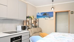 A compact kitchen with a microwave, oven, and white cabinets. There is a bed with a colorful bedspread and a chair. A painting of a beach scene is on the wall. - S378 - Sirolo, new one-bedroom apartment with garden and parking (Sirolo)