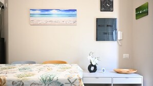 A room with a bed, a desk, a wall clock, a painting of a beach, and a vase with flowers. - S378 - Sirolo, new one-bedroom apartment with garden and parking (Sirolo)
