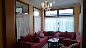 A living room with a red sofa set, a glass coffee table, and a chandelier. - Hotel Vitalia (Ushuaia)