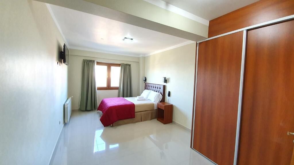 A bedroom with a bed, a nightstand, a wardrobe, and a window with curtains.