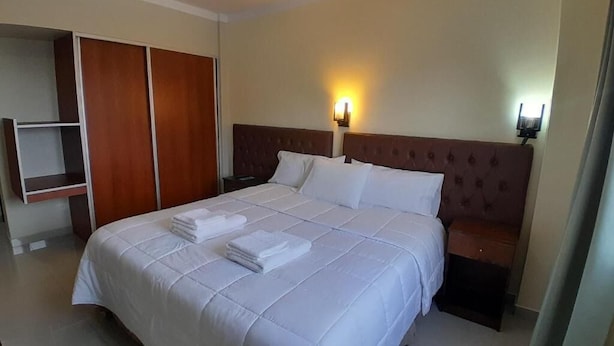 A hotel room with a large bed, a wardrobe, and a nightstand with a lamp. - Hotel Vitalia (Ushuaia)