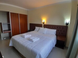 Una habitación de hotel con una cama grande, un armario y una mesita de noche con una lámpara.