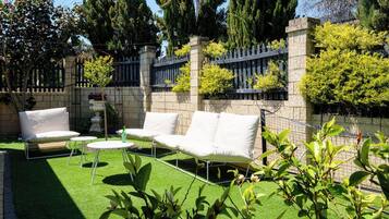 An outdoor seating area with a white sofa and two chairs, surrounded by a stone wall and greenery.