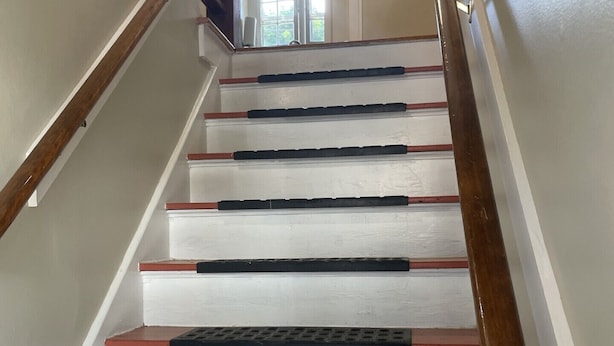A staircase with white steps and red treads, leading to a landing with a ceiling fan. - Cozy Coach House: just minutes to CMU and Soaring Eagle Casino (Mount Pleasant)