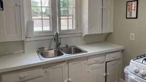 A kitchen with white cabinets, a stainless steel sink, a gas stove, and a window with a view of greenery. - Cozy Coach House: just minutes to CMU and Soaring Eagle Casino (Mount Pleasant)