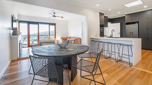 A modern kitchen with a central island, bar stools, and a dining area with a round table and wire mesh chairs. - Derwent Outlook Gateway to Scenic Trails and Beaches (Mount Nelson)