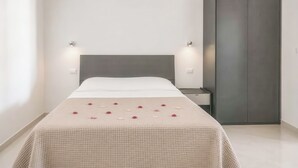 Een netjes opgemaakt bed met een witte spreidek en een beige gewatteerde deken, een nachtkastje en een kledingkast.