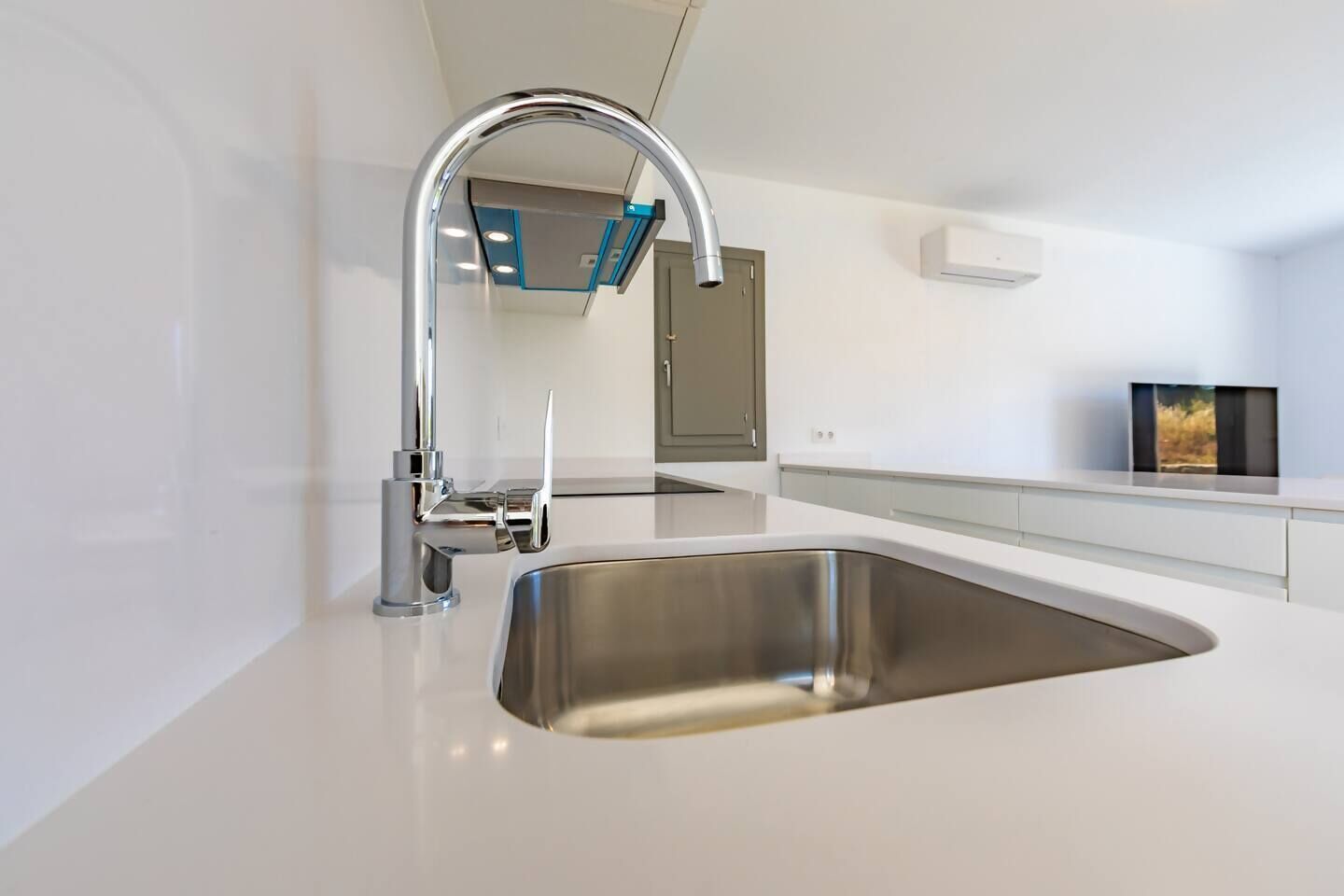 A modern kitchen with a stainless steel sink, a chrome faucet, and a white countertop.