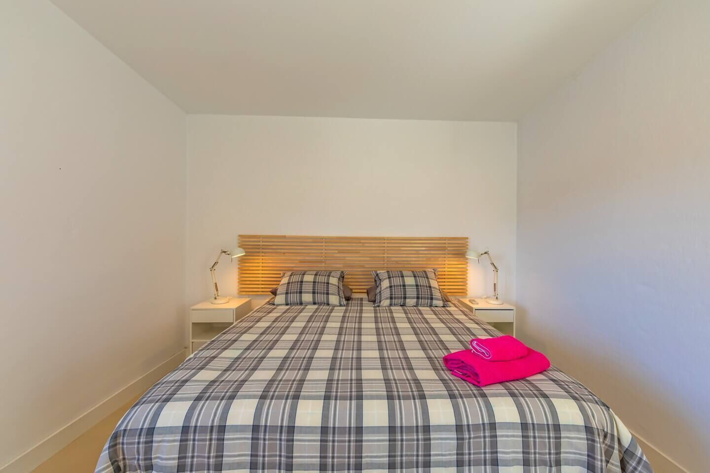 Un lit simple avec une couvre-lit à carreaux, deux lampes de chevet et une tête de lit en bois.