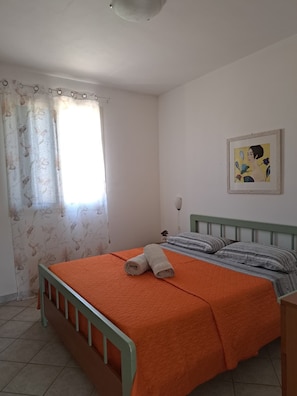 A bedroom with a bed, curtains, a painting, and a bedside lamp. - The Residences 1 (Marina di Modica)