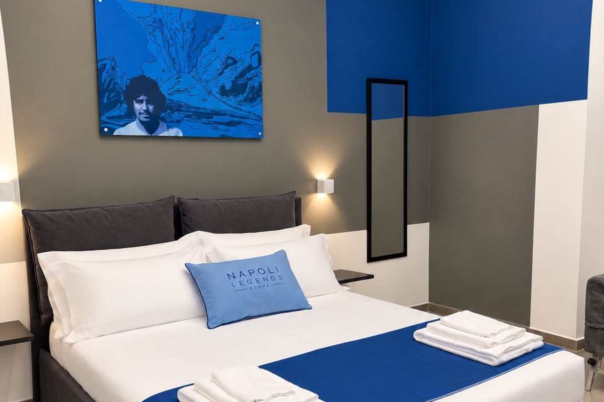 Een moderne hotelkamer met een groot bed, een blauwe accentmuur, een schilderij en een nachtkastje met een lamp.