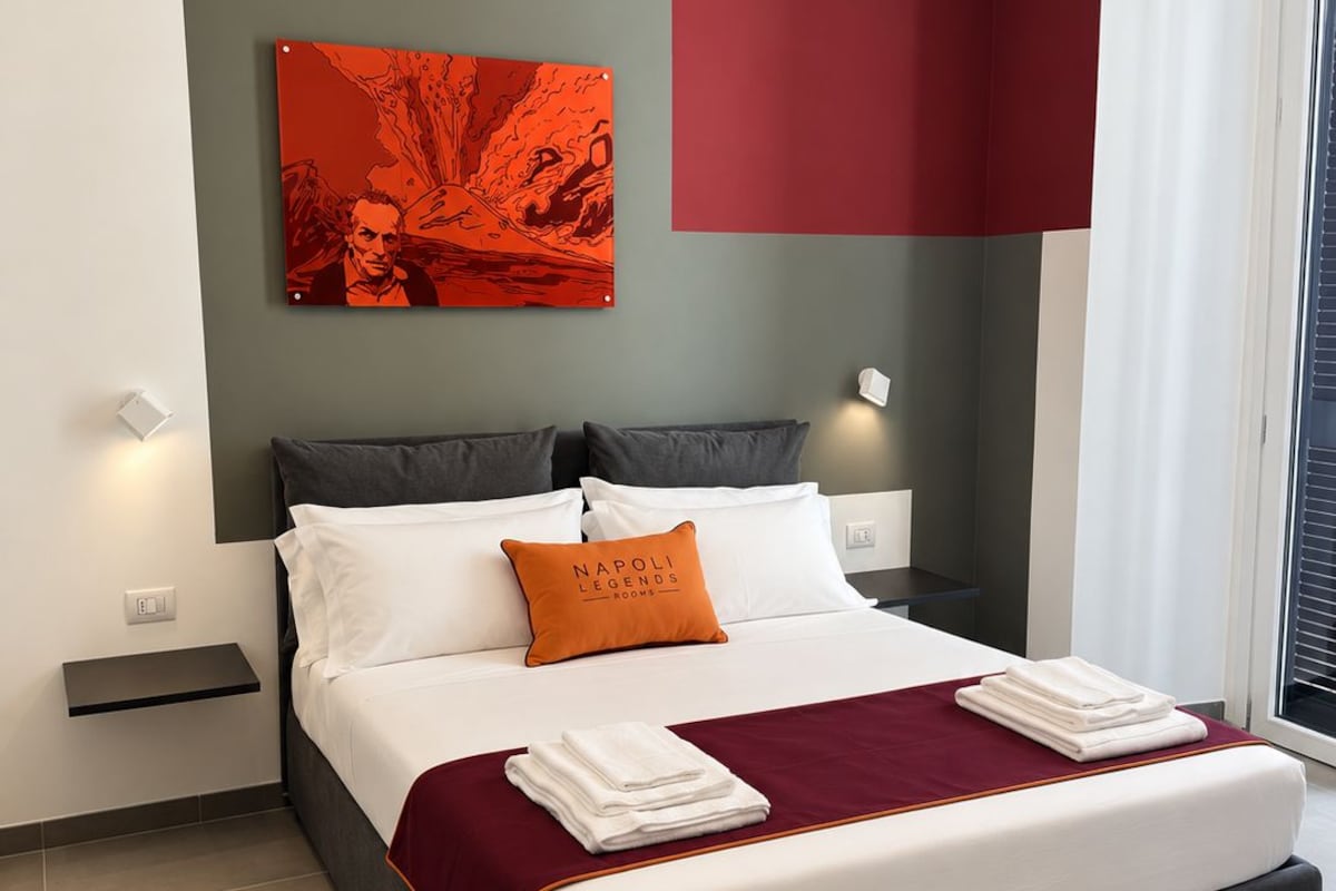 Een moderne slaapkamer met een groot bed, een rode accentmuur en een stadsgezicht op een schilderij.