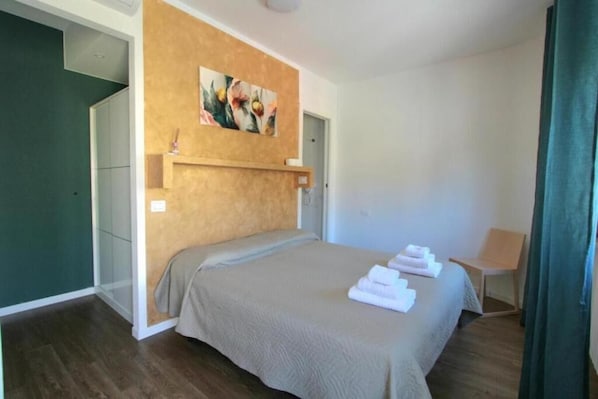 A bedroom with a bed, a painting on the wall, a chair, and a door.