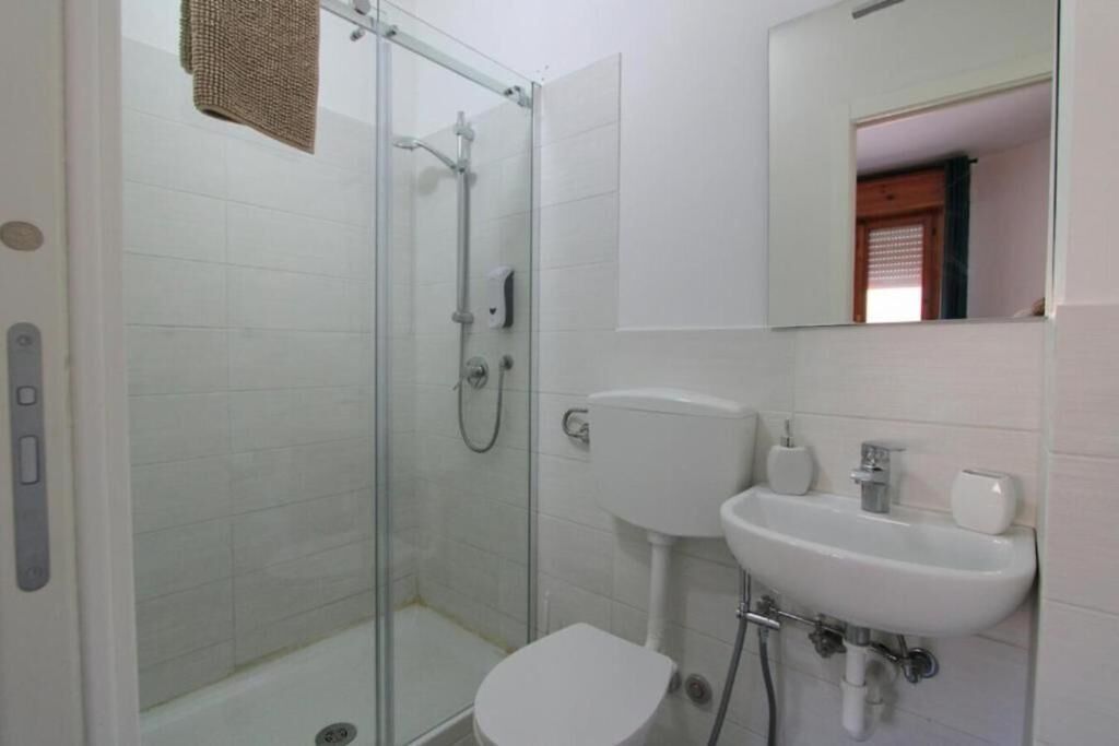 A bathroom with a glass-enclosed shower, a white toilet, and a sink with a mirror above it.