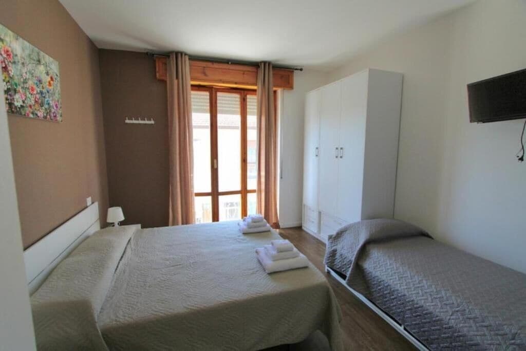 A hotel room with two beds, a wardrobe, a painting on the wall, and a window with curtains.