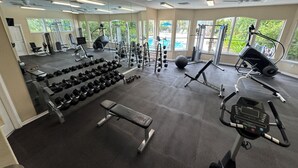 Une salle de sport équipée de divers appareils, dotée de grandes fenêtres et offrant une vue sur la verdure environnante.