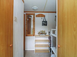 A hallway with wooden doors, a mirror, a shelf with a plant, and a hanging bag.