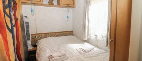 A bedroom with a bed, a heater, a window with curtains, and a door.