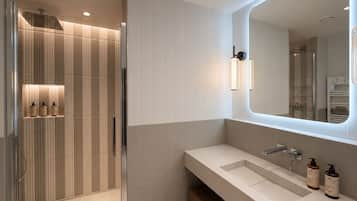 Une salle de bain moderne dotée d’une douche à l’italienne, d’un grand miroir et d’un meuble-lavabo avec un évier et des rangements.
