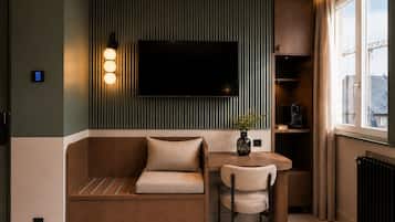 Una sala de estar moderna con un sofá, una mesa de comedor, una silla, un televisor montado en la pared y un ventanal con cortinas.