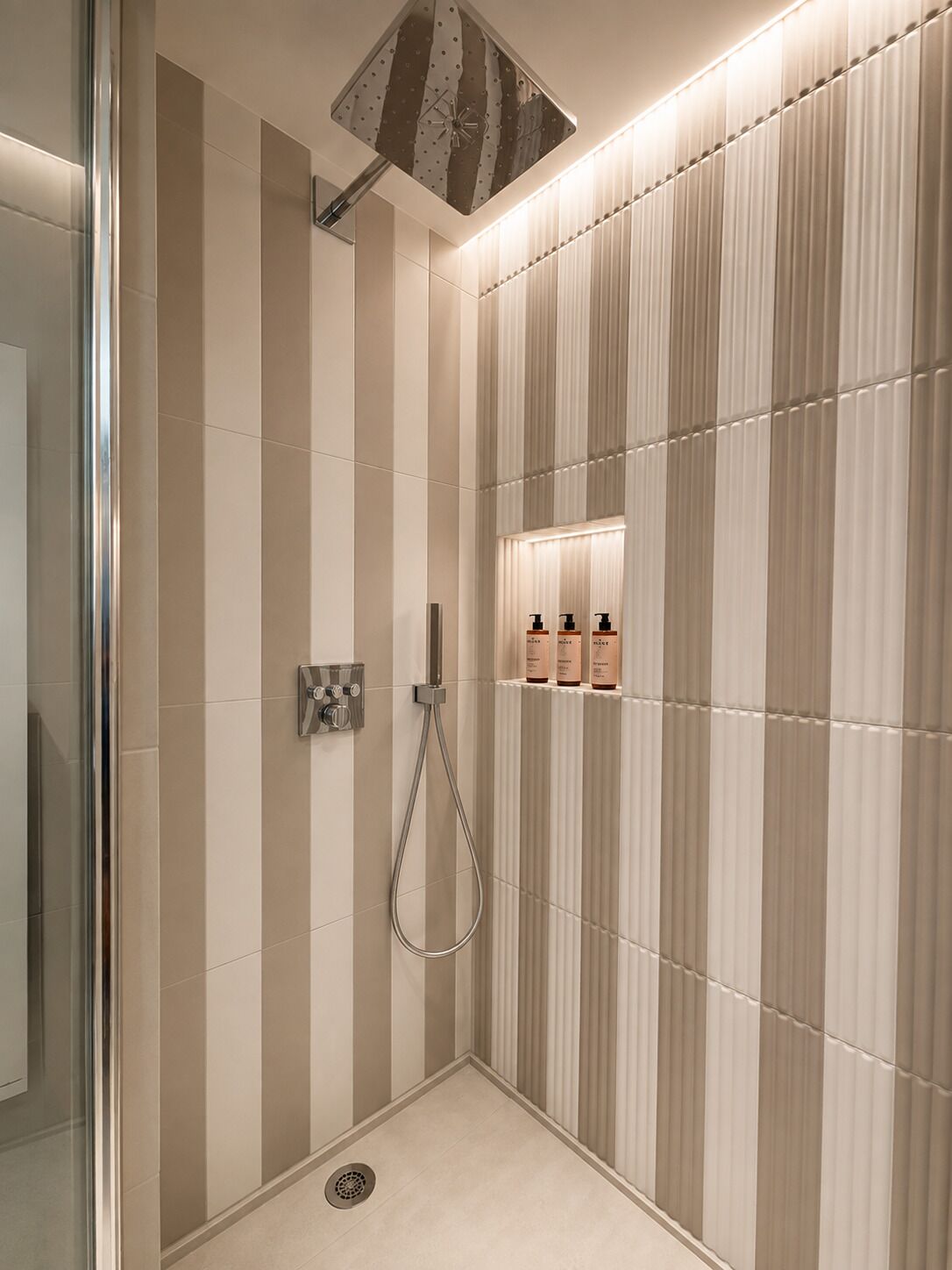 A modern bathroom with a shower, a glass door, and a wall-mounted shelf with toiletries.