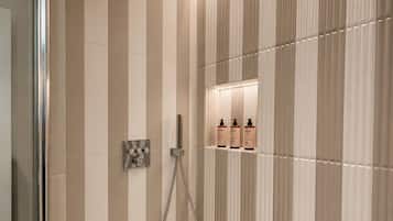 A modern bathroom with a shower, a glass door, and a wall-mounted shelf with toiletries.