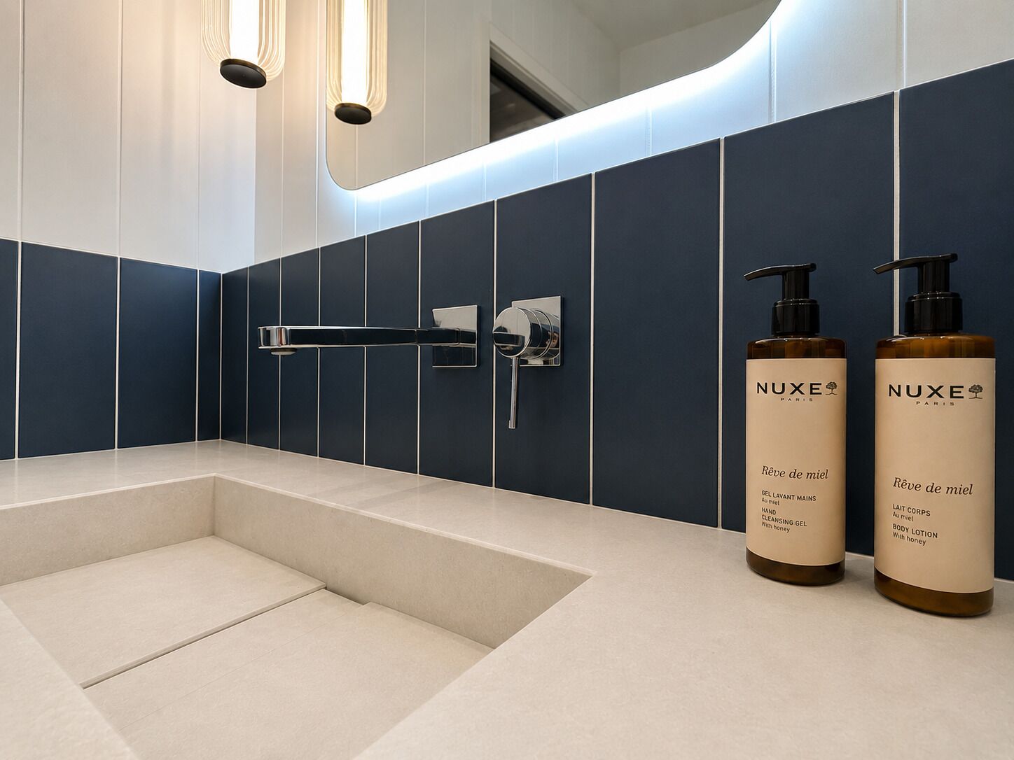 Un baño moderno con una bañera, una ducha de mano y dos botellas de crema corporal Nuxe Paris.