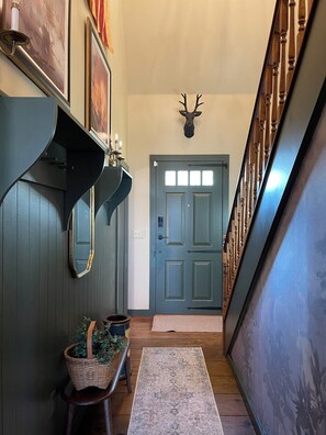 A hallway with a wooden staircase, a door with a deer head decoration, and a mirror on the wall.